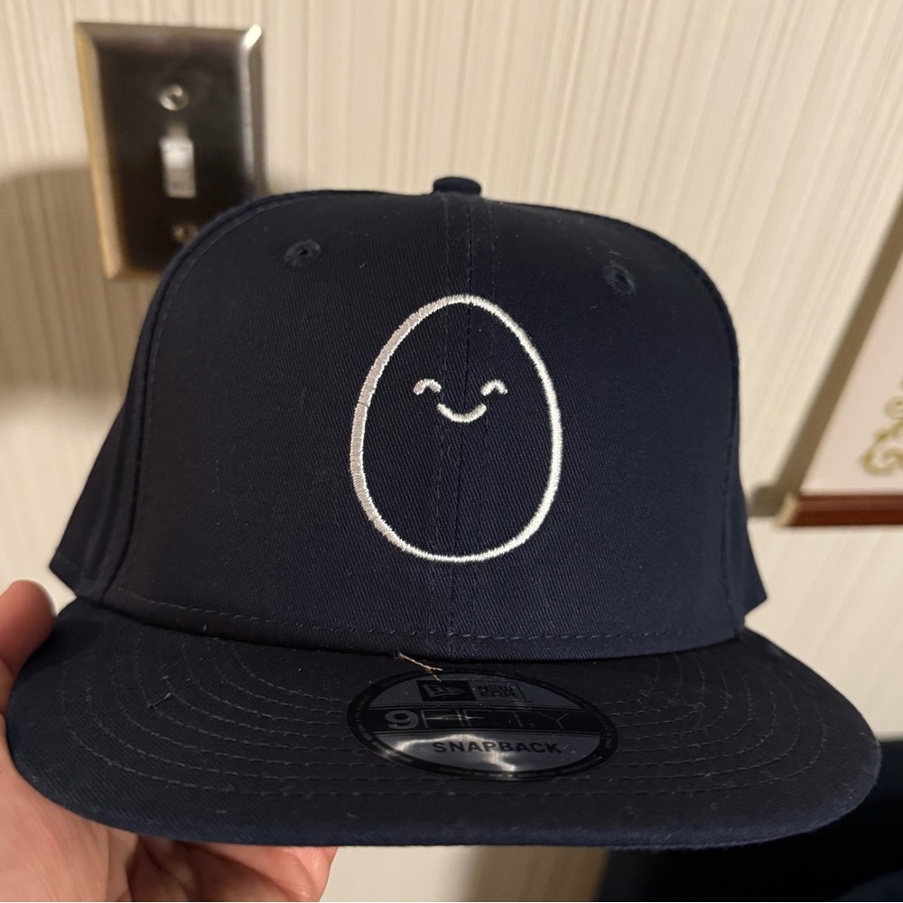 Smiling egg flat billed navy blue New Era snap back hat. NWT. Unworn.